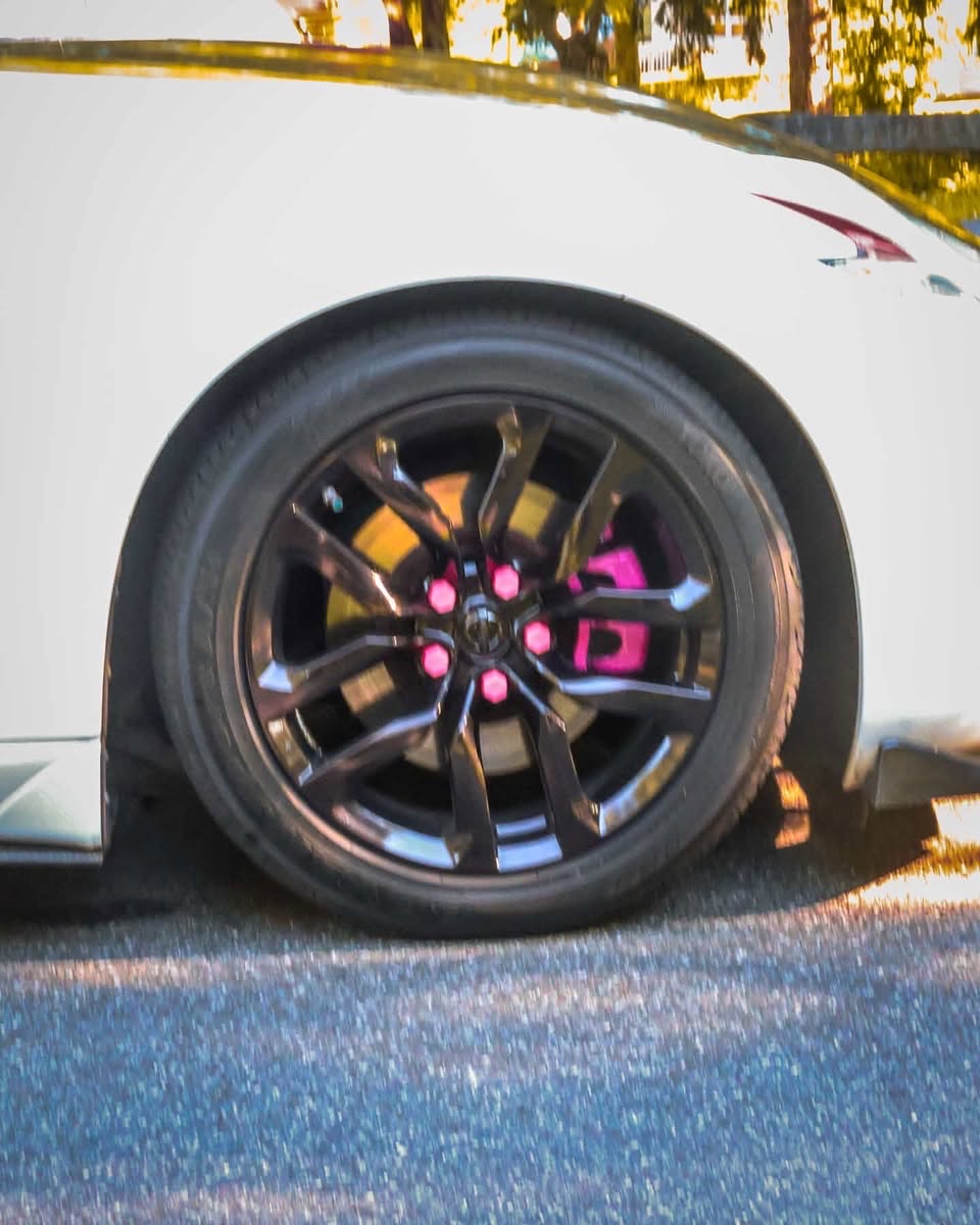Detail of a black split-spoke wheel with pink lug nuts and a bright pink brake caliper behind the spokes.