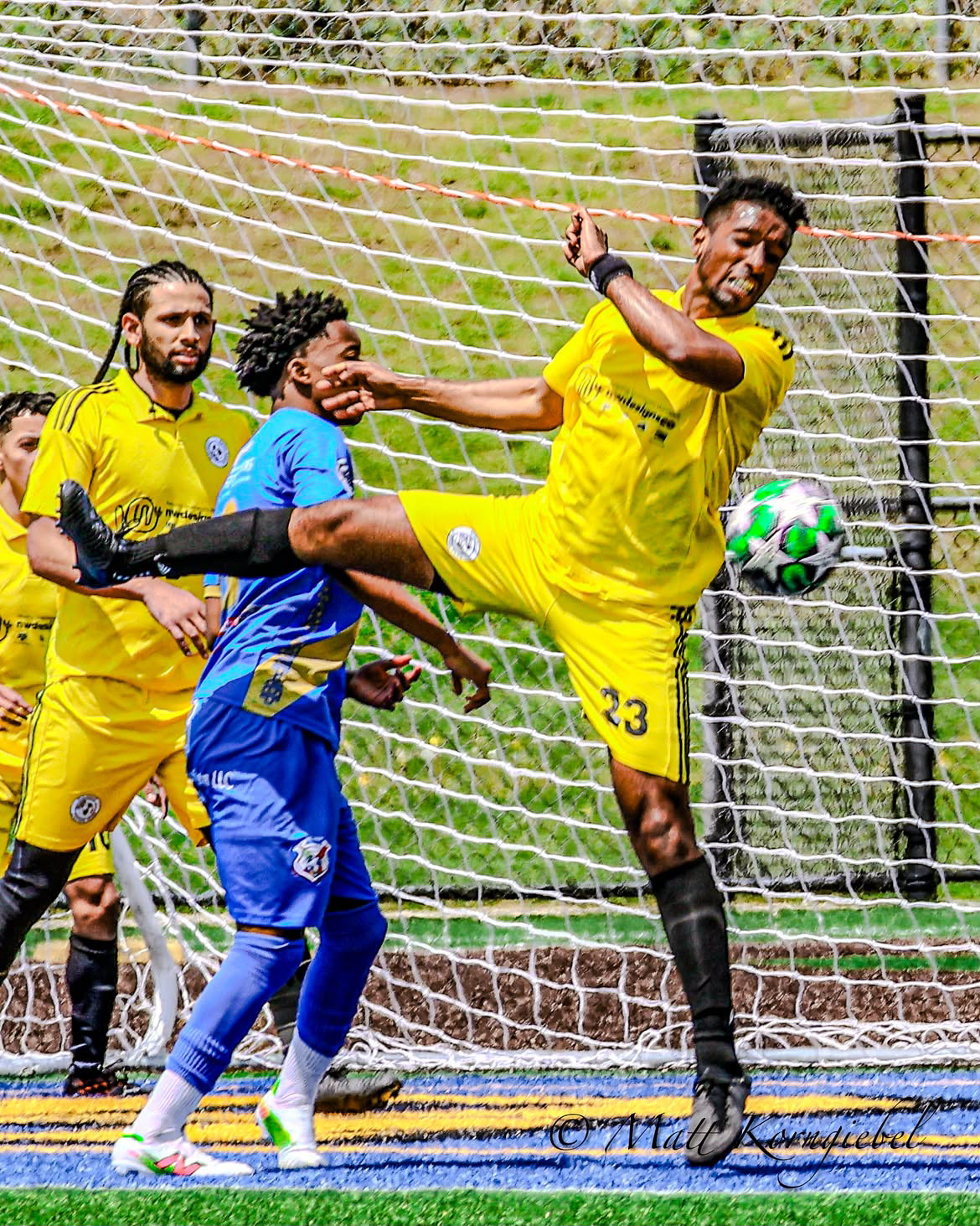 Defender in yellow stretching high in the six-yard box to clear a bouncing ball off the line.